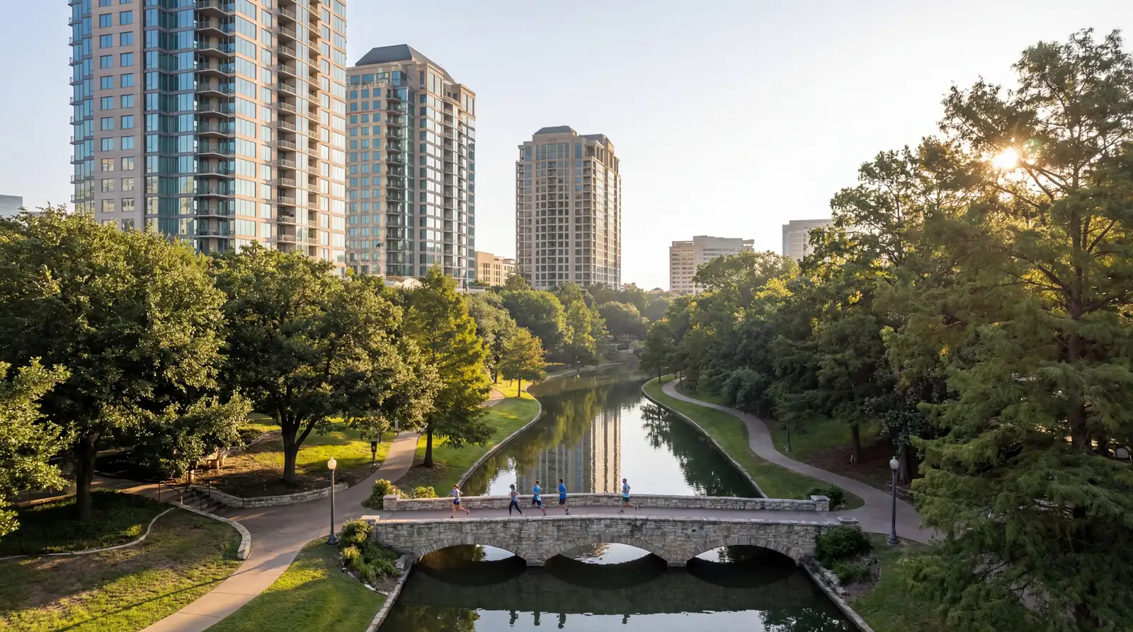 Turtle Creek Dallas luxury high-rise condos along winding waterway with stone bridge, joggers, and lush parkland