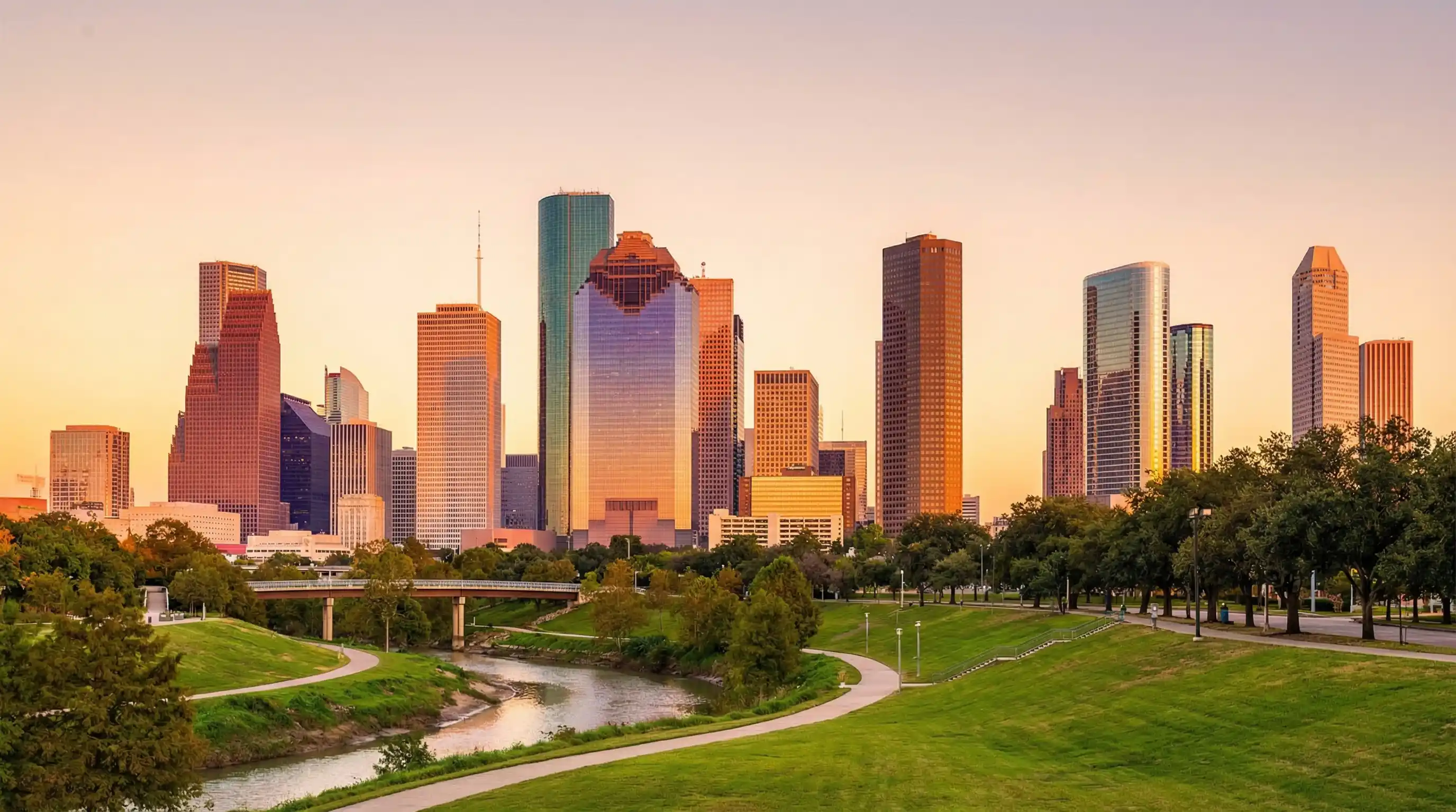 Houston Texas downtown skyline at golden hour viewed from Buffalo Bayou Park with green parkland and bayou in foreground